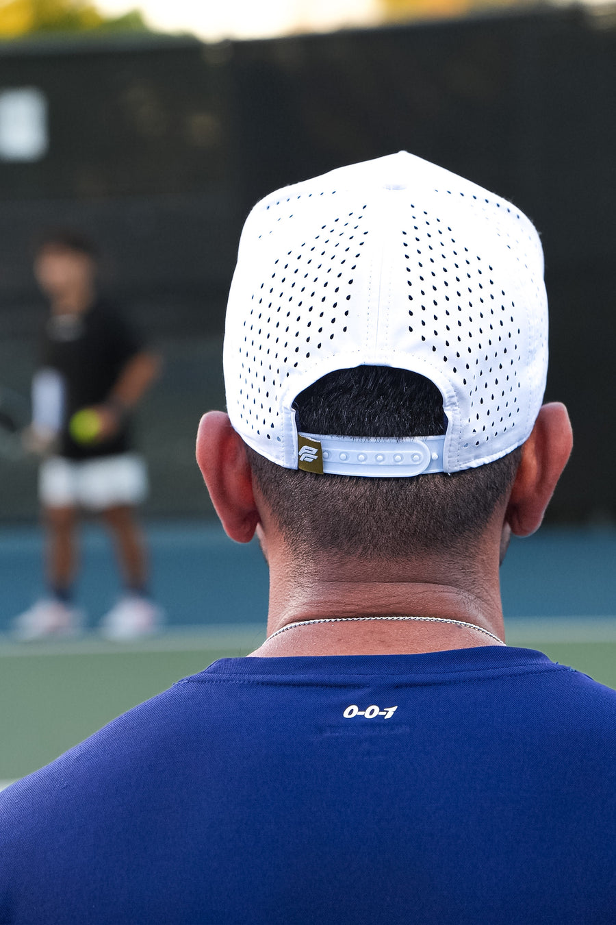 Person wearing a white cap with black logo on a tennis court, navy
