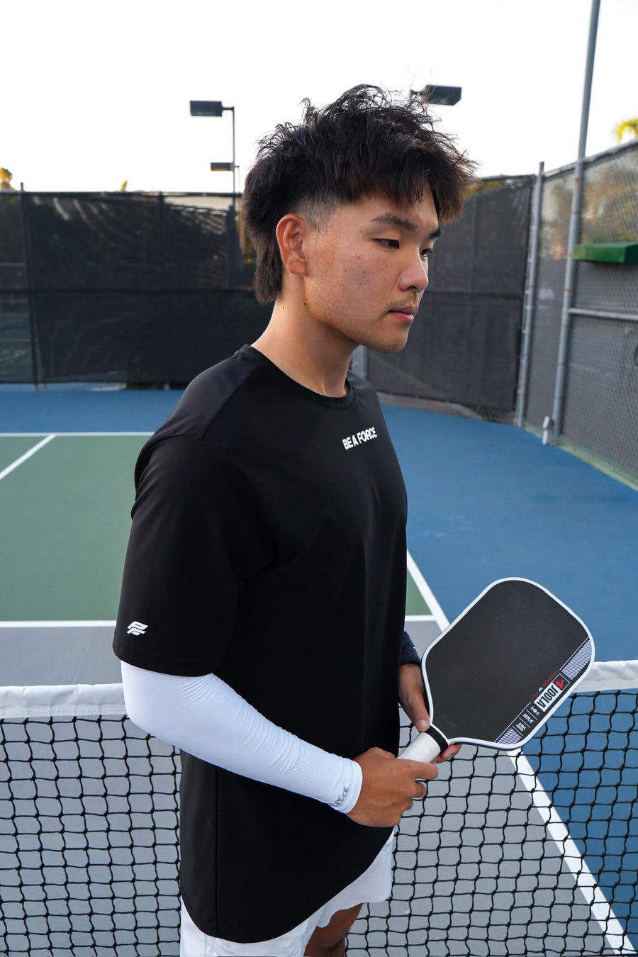 Person holding a pickleball paddle on a court, black