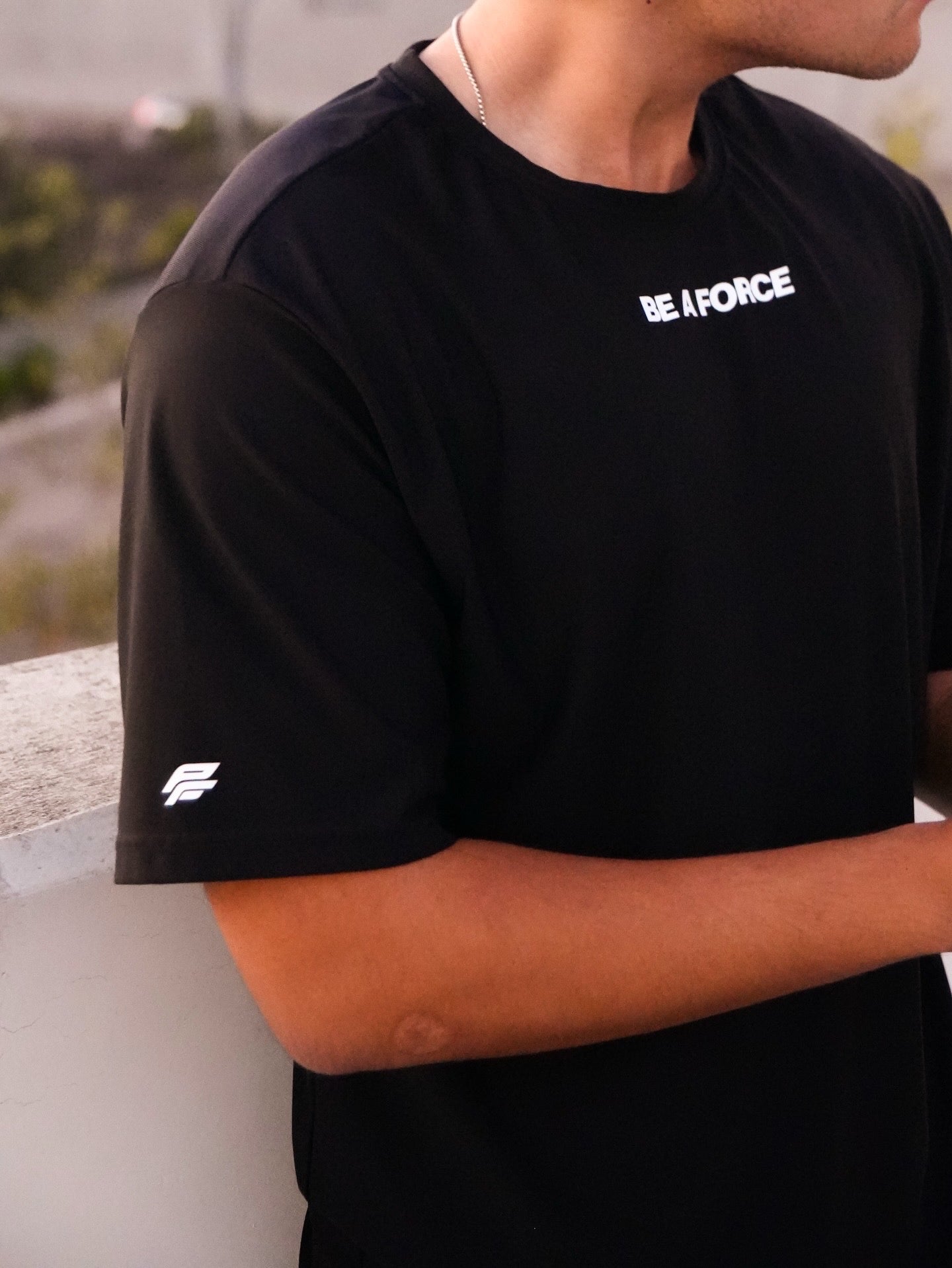 Person wearing a black t-shirt with 'BE A FORCE' text, standing outdoors, black