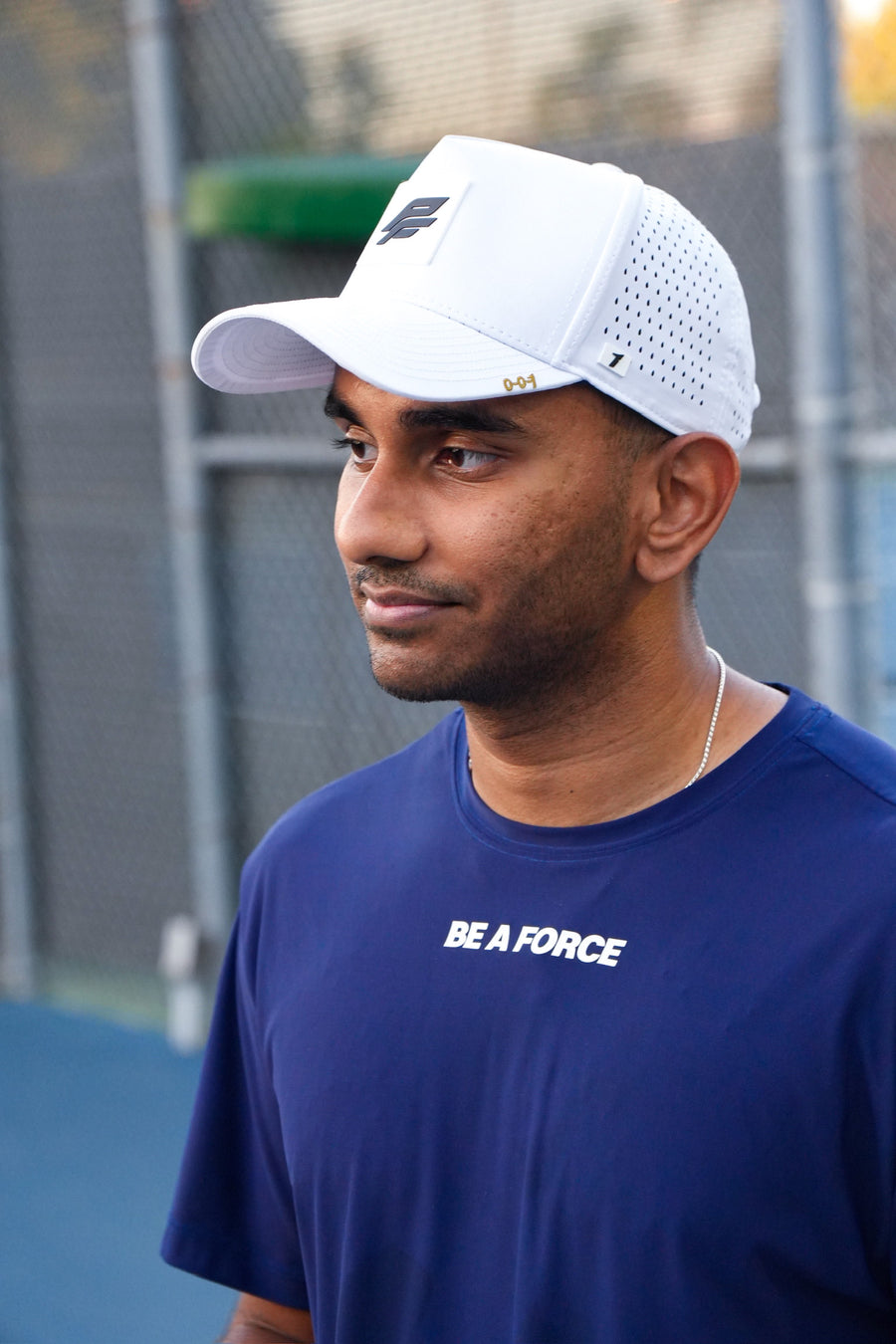 Man wearing a white cap and blue shirt with text on a tennis court, navy