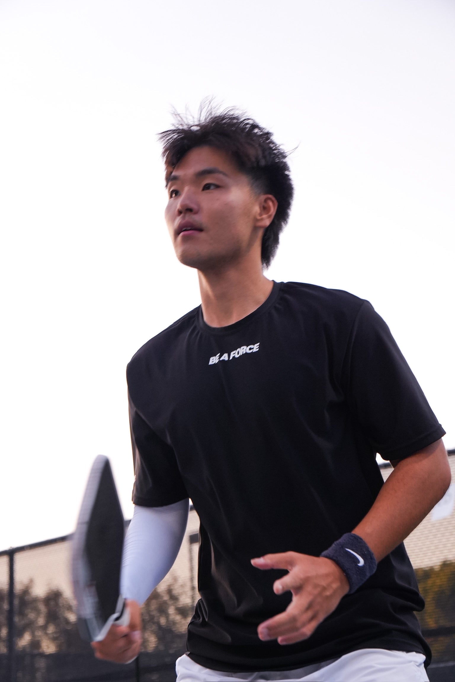 Person holding a paddle on a sports court wearing a black shirt with visible branding, black